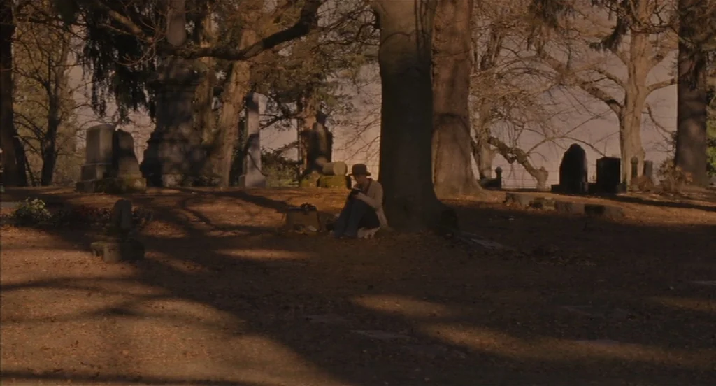 Restless (2011) movie still: wide — A spacious cemetery features numerous scattered headstones among tall, bare-branched autumn trees. A solitary…