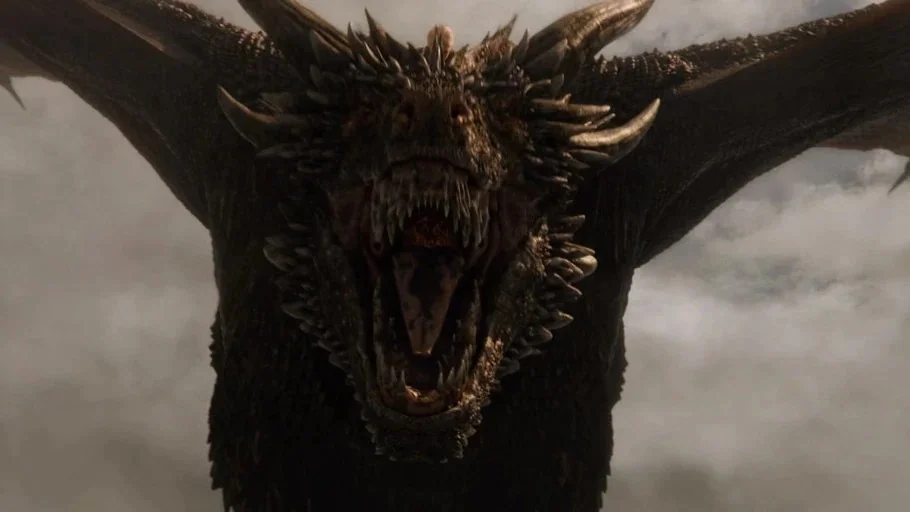 Game of Thrones (2017) movie still: closeup — A massive dragon flies through a cloudy, grey overcast sky. The dragon approaches the camera with its…