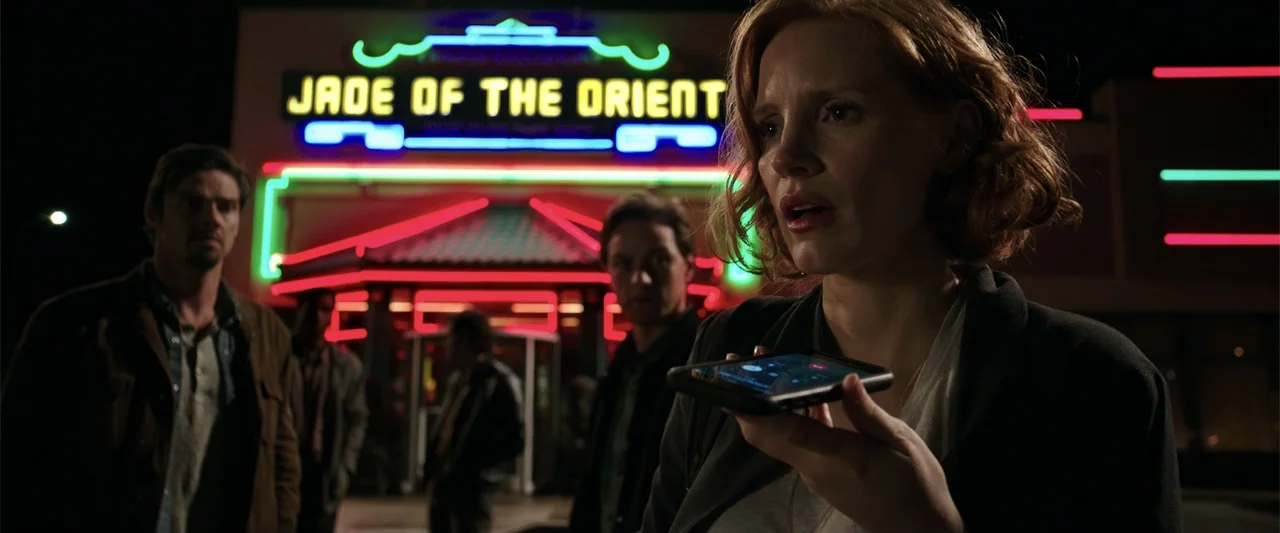 K.G.F: Chapter 2 (2022) movie still: medium — A dark outdoor parking lot at night features a glowing neon sign for a business. A woman speaks on her…