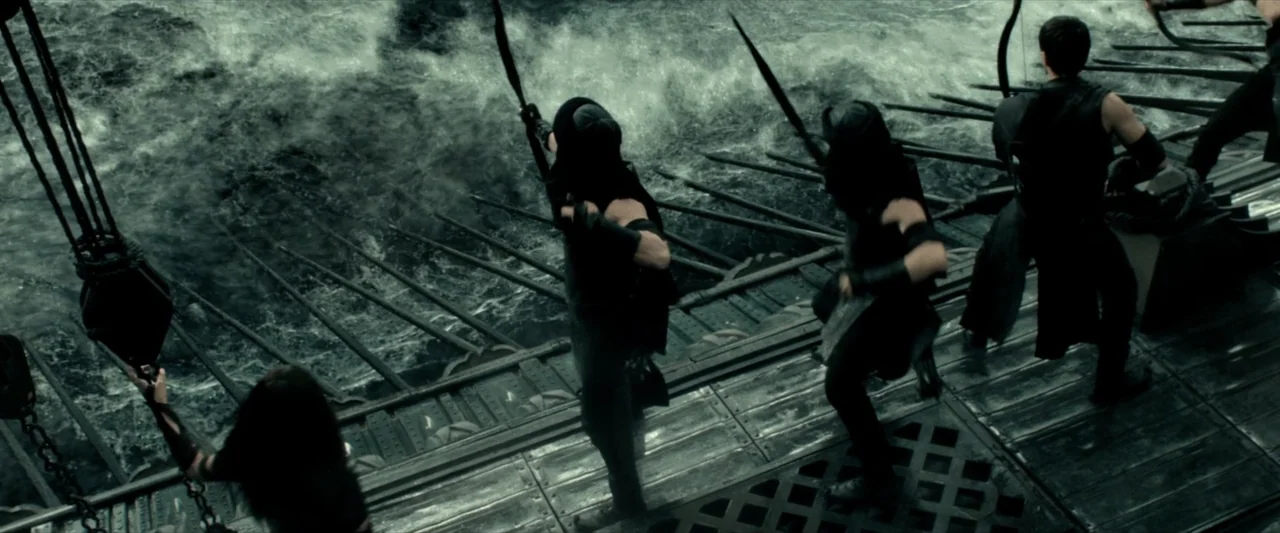 300: Rise of an Empire (2014) movie still: wide — A wooden warship deck is crowded with archers facing a turbulent dark ocean. The soldiers hold…