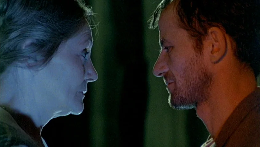 Almanac of Fall (1984) movie still: closeup — Two individuals stand in a dimly lit, nondescript interior space. They face one another in profile…