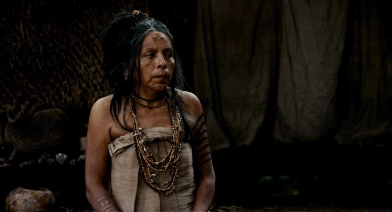 Apocalypto (2006) movie still: medium — An outdoor encampment at night with draped fabric structures in the background. A woman wearing tribal…