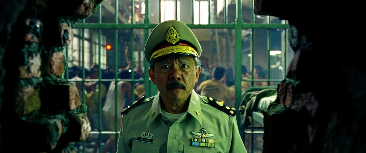 The Hangover Part III (2013) movie still: medium — A cluttered space behind green metal bars separates the subject from a crowded background. A…