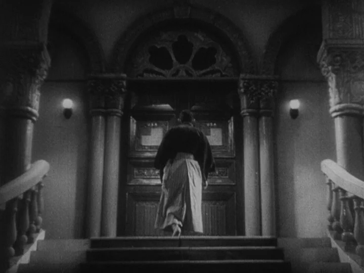 Sanshiro Sugata Part II (1945) movie still: fullbody — A stone building entrance features a large wooden door beneath an arched masonry frame. A man…