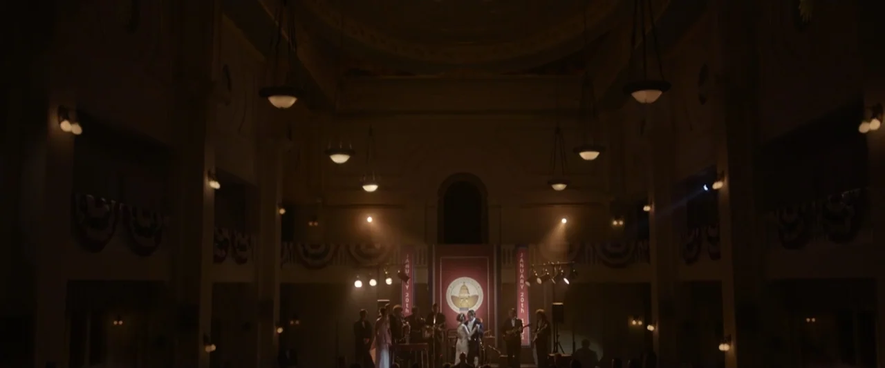 Reagan (2024) movie still: establishing — A dark, expansive ballroom features hanging pendant lights and decorative banners for an event. A small…