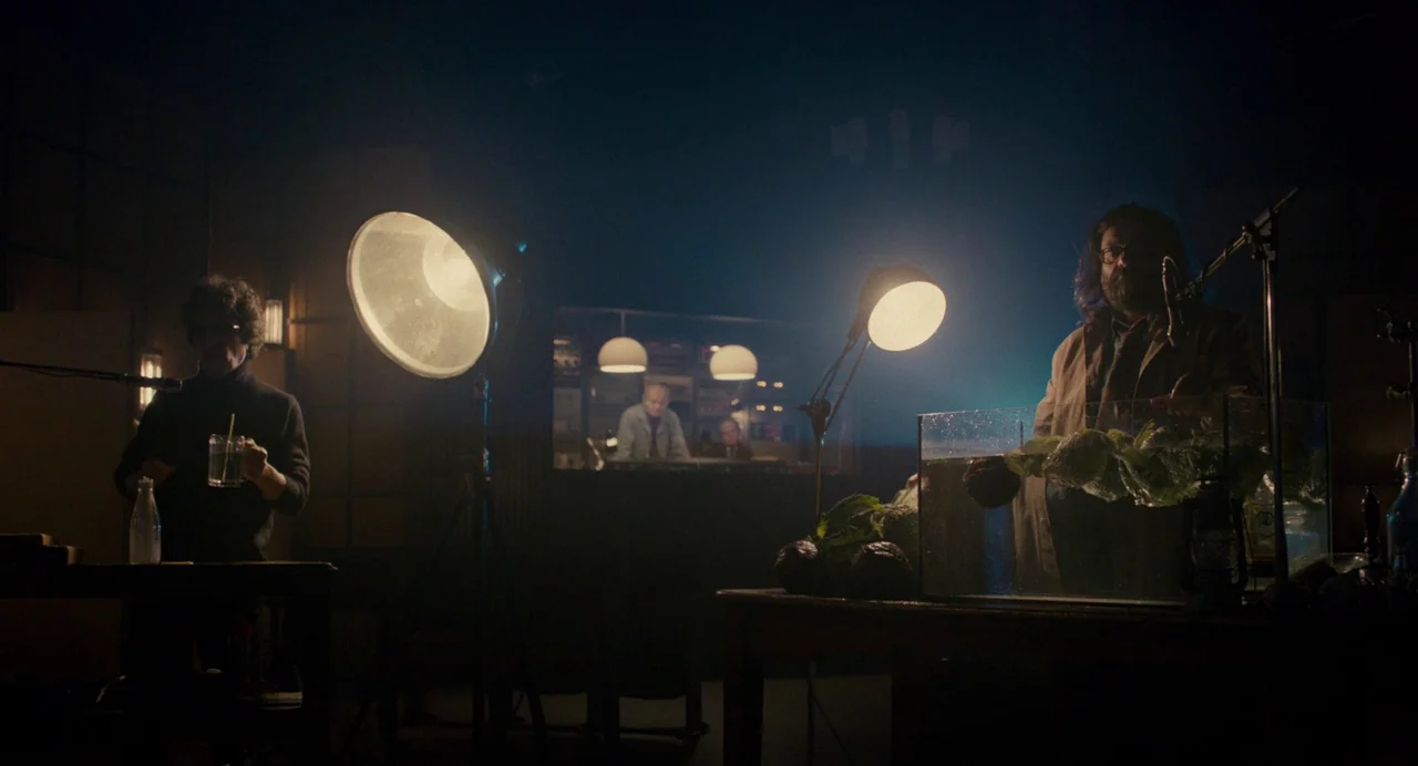 Berberian Sound Studio (2012) movie still: wide — A dark recording studio with large lamps and vintage electronic equipment in the background. Two…