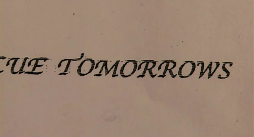 Inland Empire (2006) movie still: closeup — A close-up shot focuses on typed black text against a beige paper surface. The words 'CUE TOMORROWS'…
