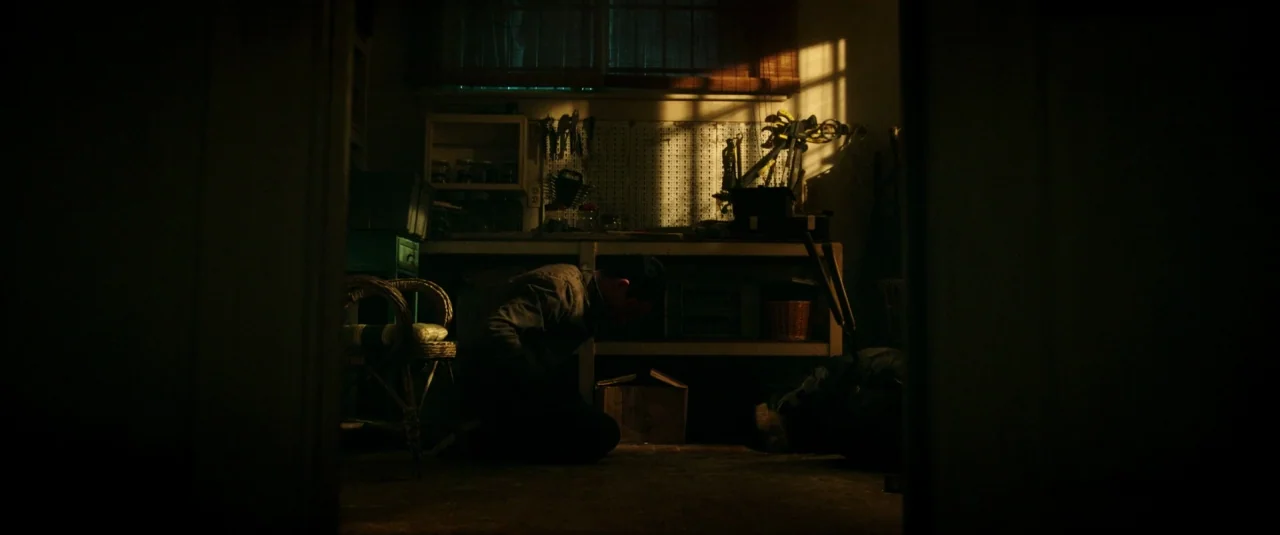 Don’t Breathe (2016) movie still: medium — A basement workshop contains a cluttered workbench with tools organized on a pegboard wall. A man kneels…