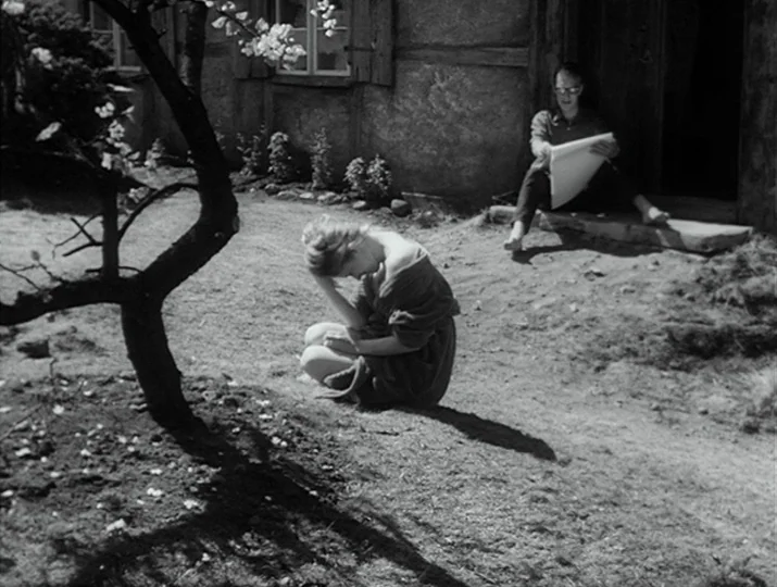 Hour of the Wolf (1968) movie still: wide — A dirt area sits before an old timber-framed house with small window panes. A woman crouches near a tree…