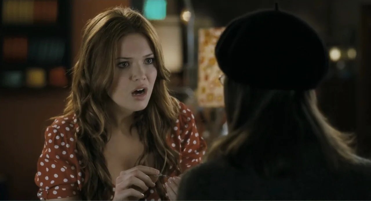 Because I Said So (2007) movie still: medium — A dimly lit indoor space features a woman in a red polka-dot blouse speaking intently. A person…