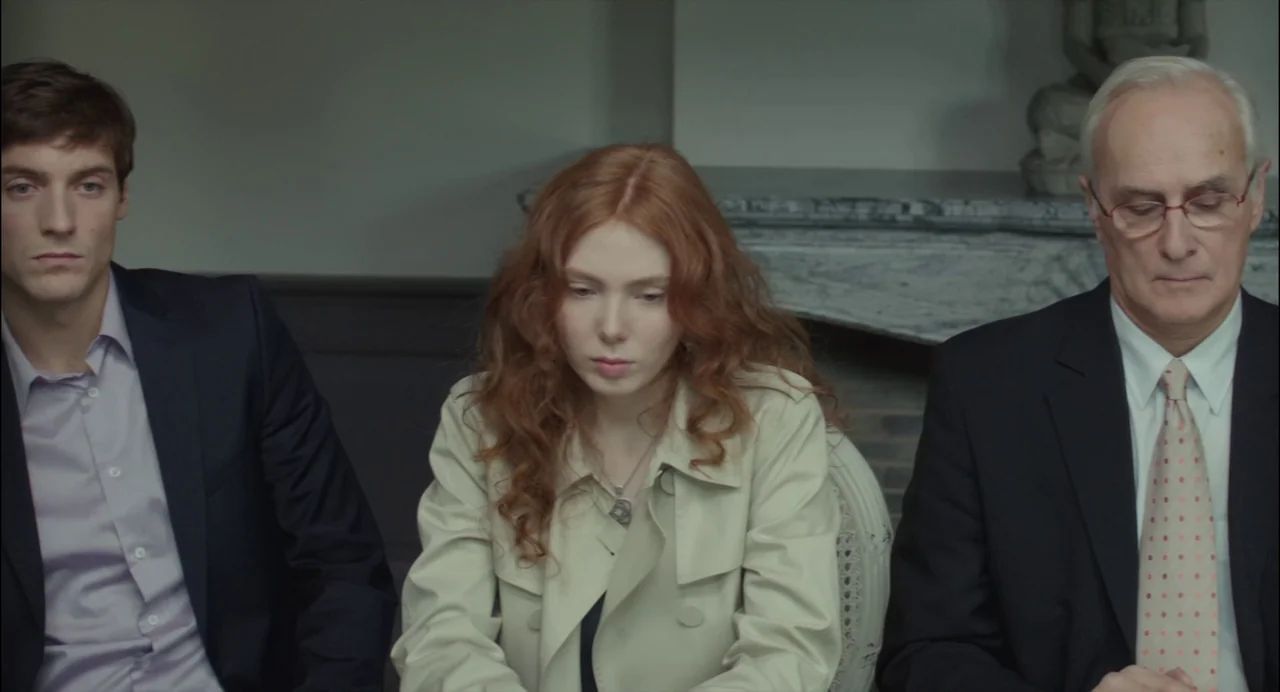 Abuse of Weakness (2013) movie still: medium — A formal interior with a marble fireplace mantel visible behind the seated people. Three people sit…