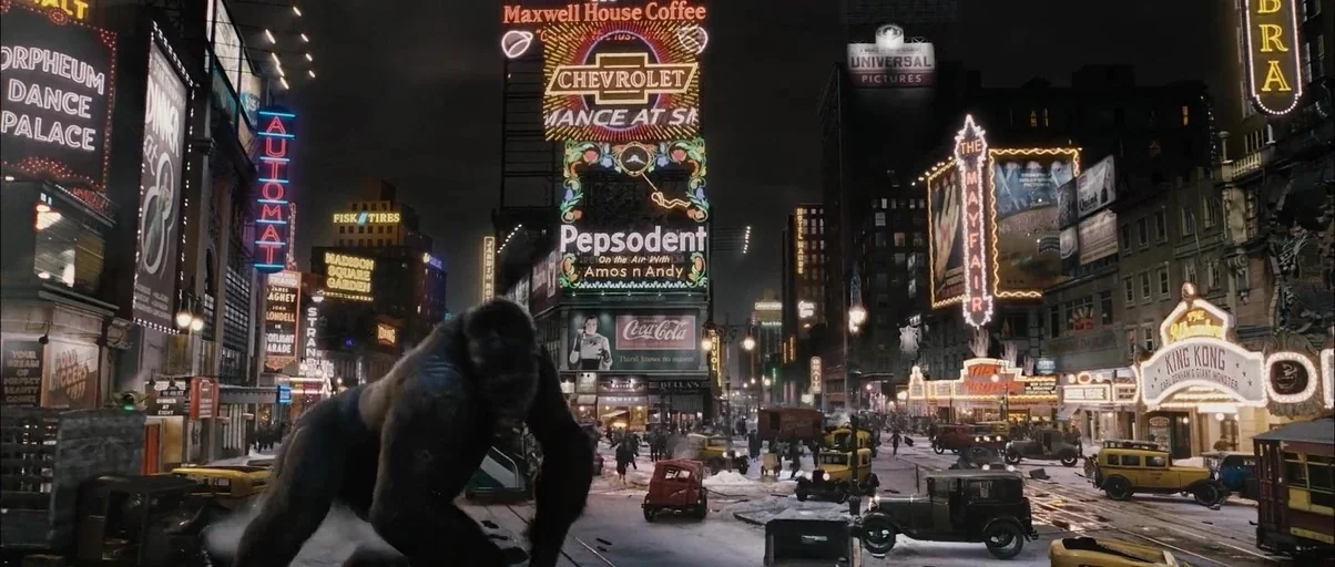 King Kong (2005) movie still: wide — A 1930s urban intersection illuminated by bright neon advertisements and period signage. A large gorilla…