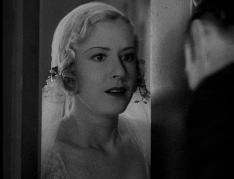 Frankenstein movie still: closeup — A woman in a bridal veil looks through a narrow opening between two walls. She stares toward an unseen person…