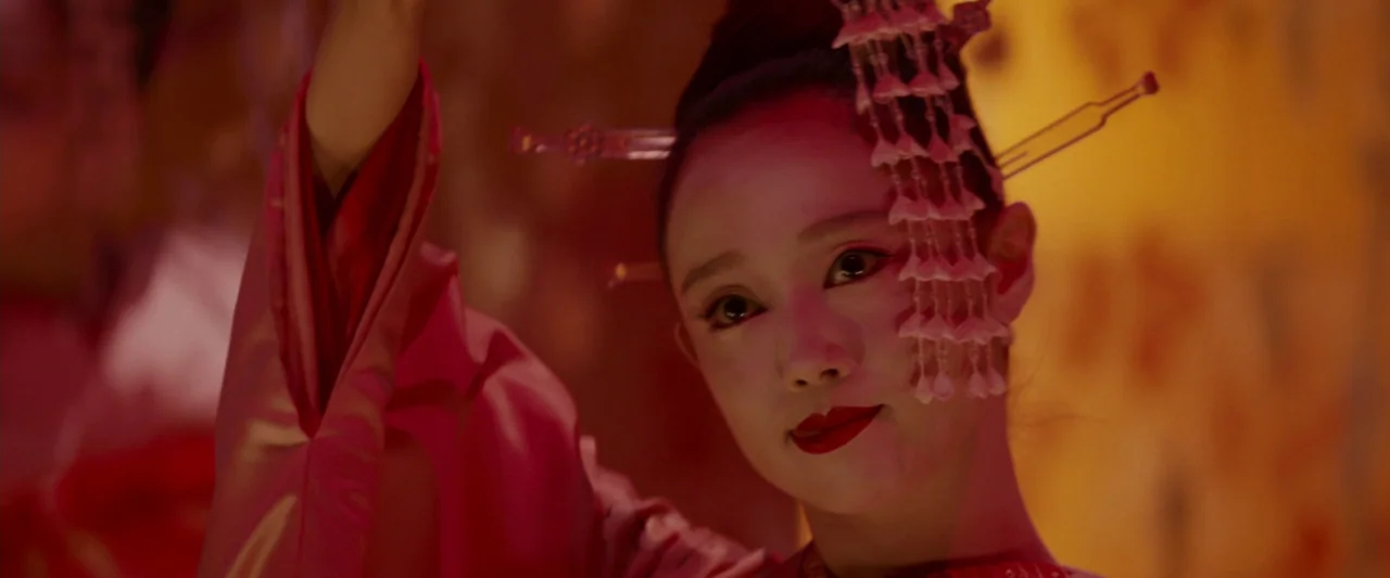 Memoirs of a Geisha (2005) movie still: closeup — A performer stands on a stage against a softly glowing golden-orange backdrop. The woman wears…