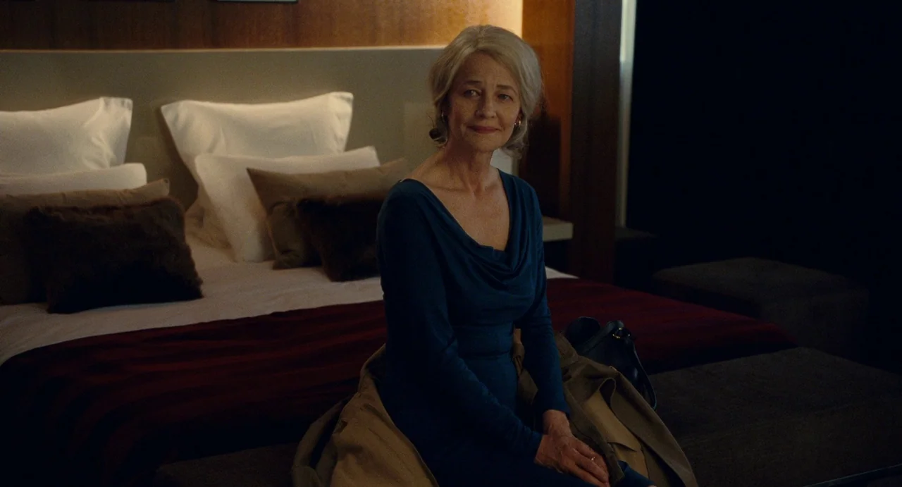 Young & Beautiful (2013) movie still: medium — A dimly lit hotel room features a plush bed with layered pillows and brown linens. A mature woman…