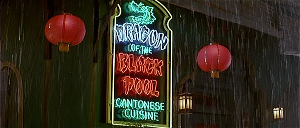 Big Trouble in Little China (1986) movie still: wide — A dark, wet exterior wall features a vertical neon sign for a restaurant. Heavy rain streaks…