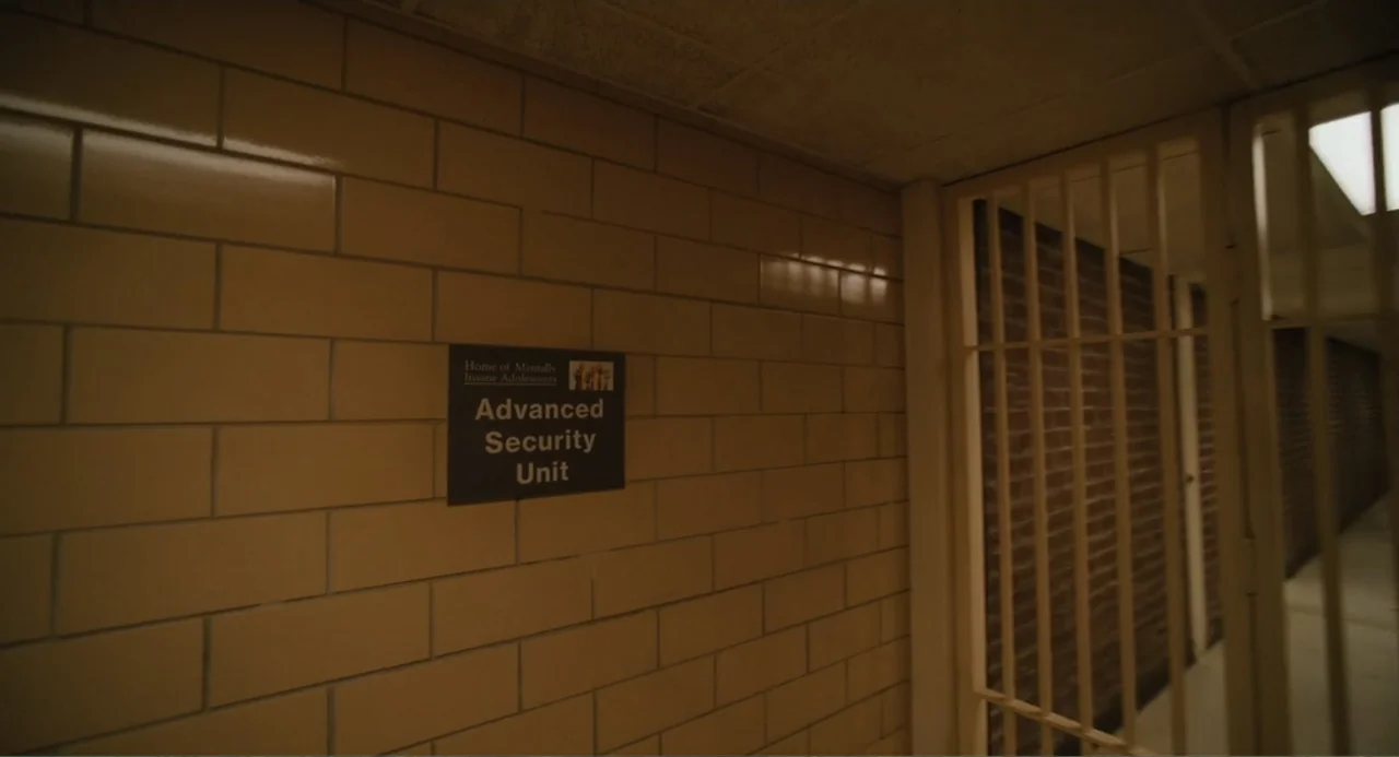 Mona Lisa and the Blood Moon (2022) movie still: medium — An interior hospital or detention facility corridor with tan glazed brick walls. A black…