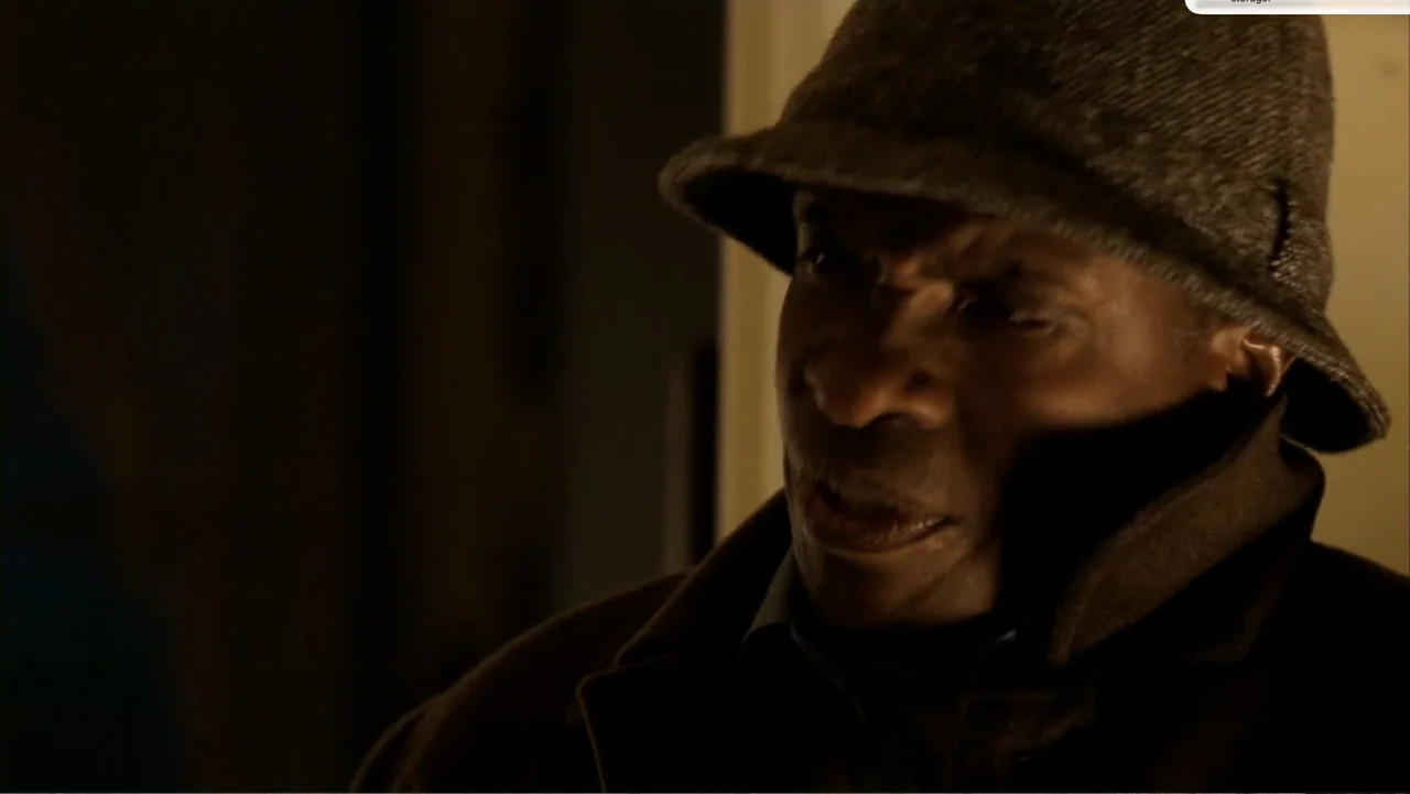 Chain Letter (2010) movie still: closeup — A dimly lit indoor space with low-key lighting highlighting the subject's face. An older man wearing a…