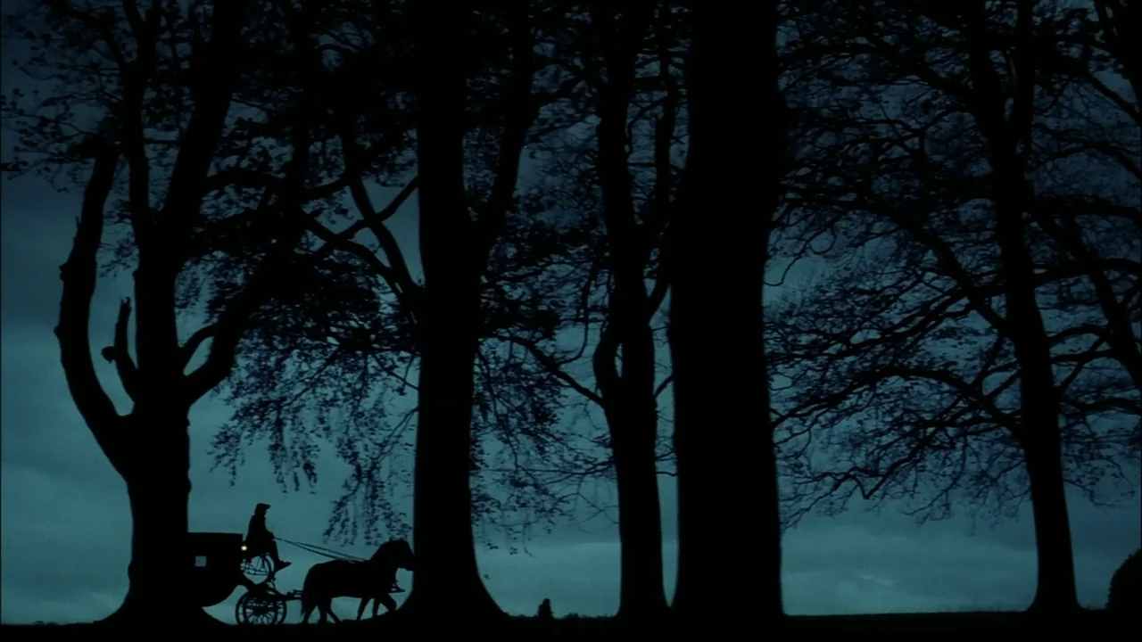 Sleepy Hollow (1999) movie still: wide — A dark row of leafless trees stands against a deep blue night sky. A horse-drawn carriage moves slowly…
