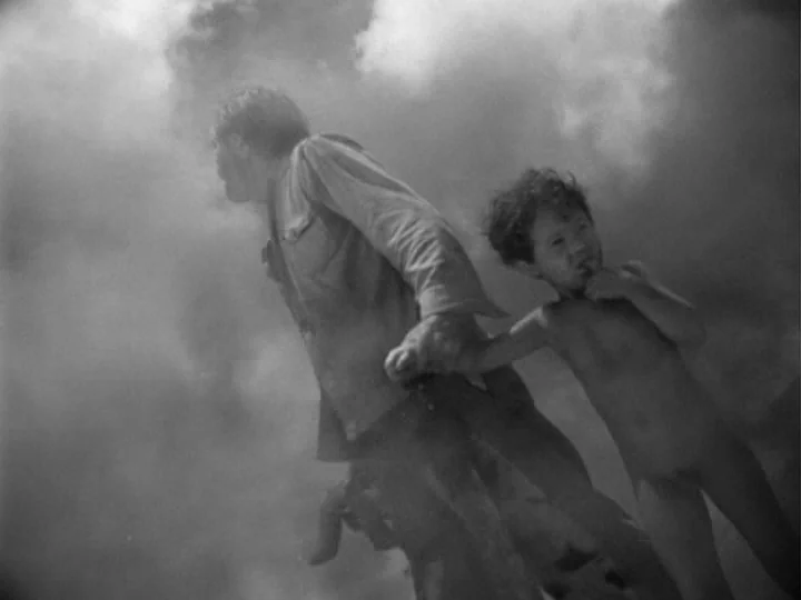 I Am Cuba (1964) movie still: medium — An open outdoor space filled with dense fog or smoke under an overcast sky. A man in a shirt walks alongside…