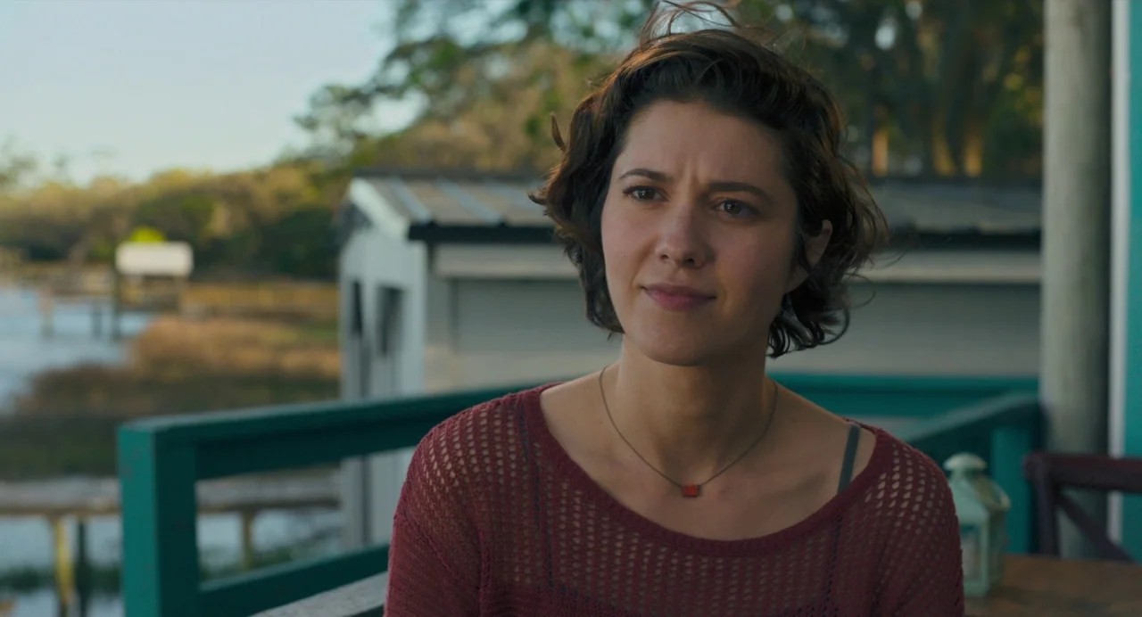 Gemini Man (2019) movie still: medium — A woman sits on an outdoor porch with a turquoise railing overlooking a marsh. She looks slightly to the…