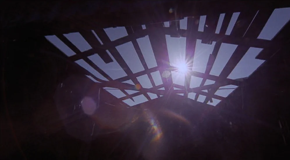 Easy Rider (1969) movie still: establishing — A dilapidated wooden ceiling with broken slats creates a grid pattern against the sky. The bright sun…