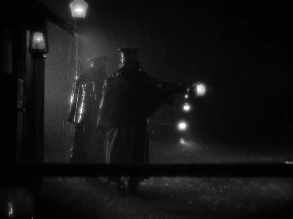 It Happened One Night (1934) movie still: medium — A dark outdoor platform during a heavy rainstorm with visible water droplets in air. Two…