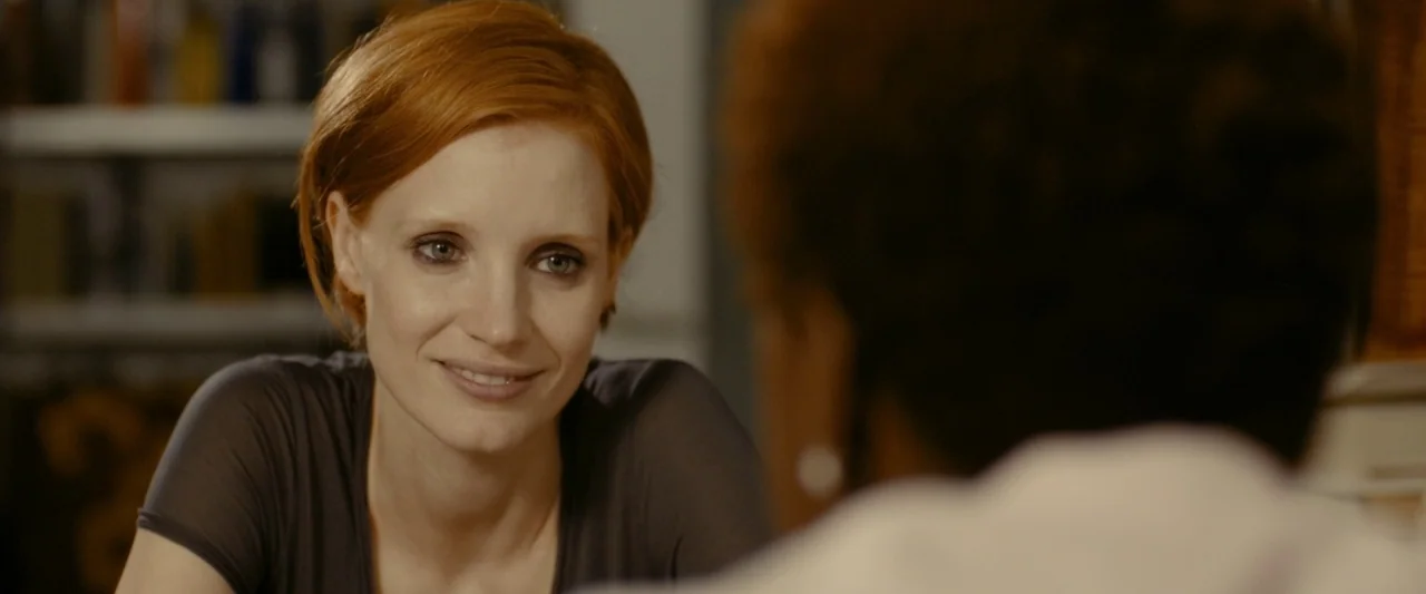The Disappearance of Eleanor Rigby: Her (2014) movie still: closeup — A woman sits in a room with blurred shelving visible in the background. She…