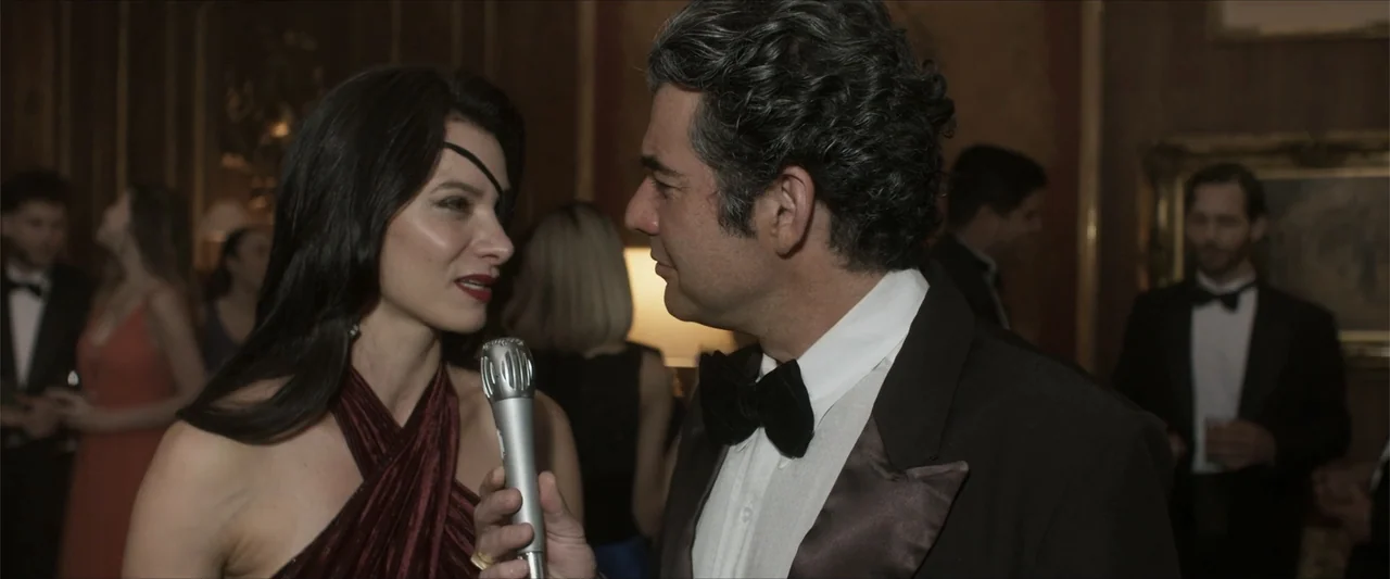 Angela (2023) movie still: medium — A crowded, dimly lit interior room with formal decor and several guests in formal attire. A woman with an eye…
