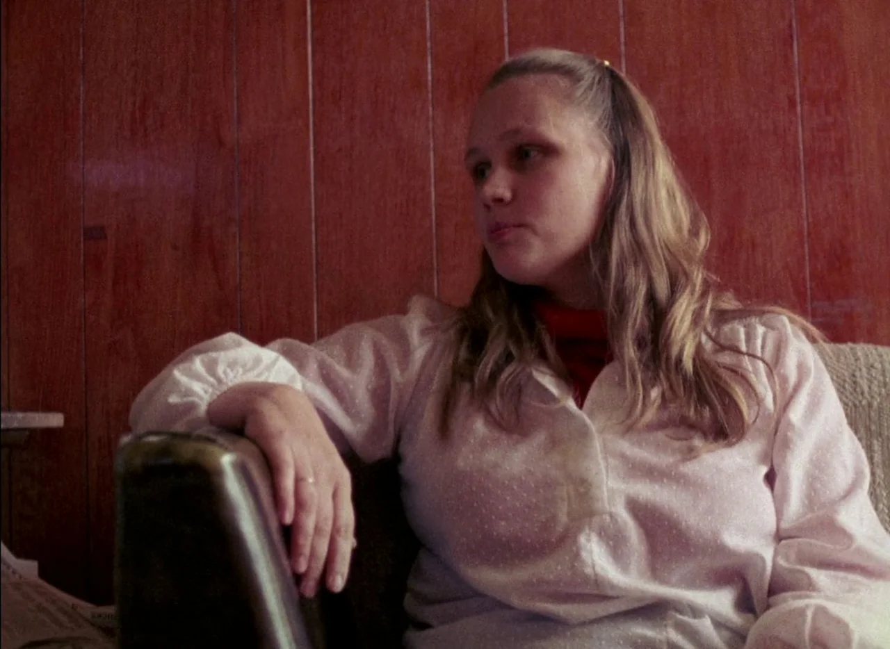 Streetwise (1984) movie still: medium — A residential room features walls covered in vertical wood paneling. A young woman sits on a cushioned…