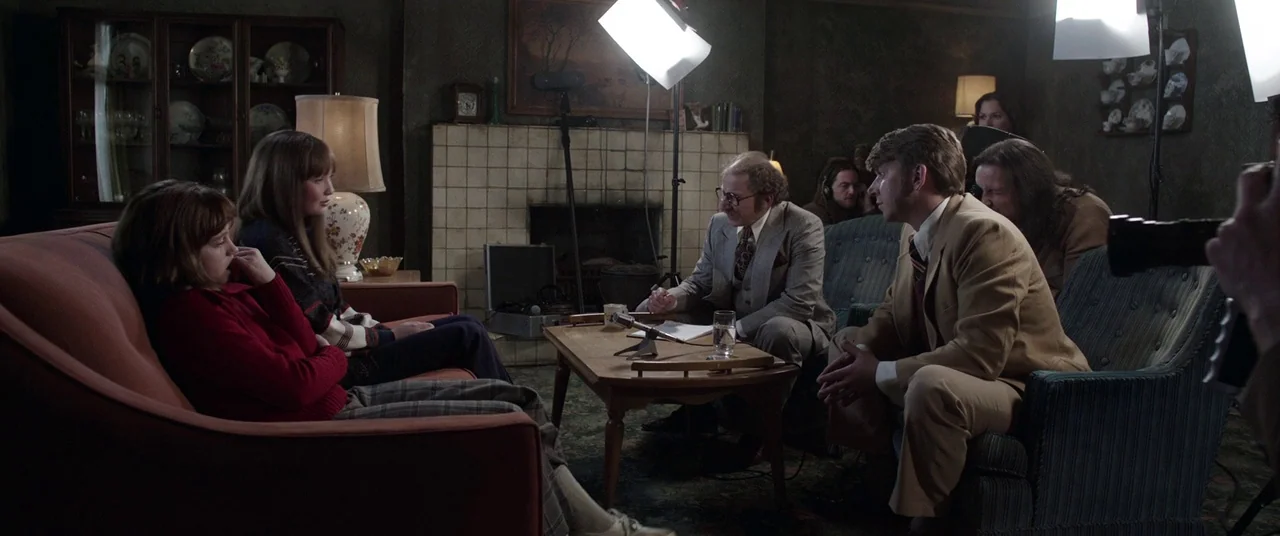 The Conjuring 2 (2016) movie still: medium — A dimly lit room furnished with vintage 1970s style furniture and a stone fireplace. A man in a tan…