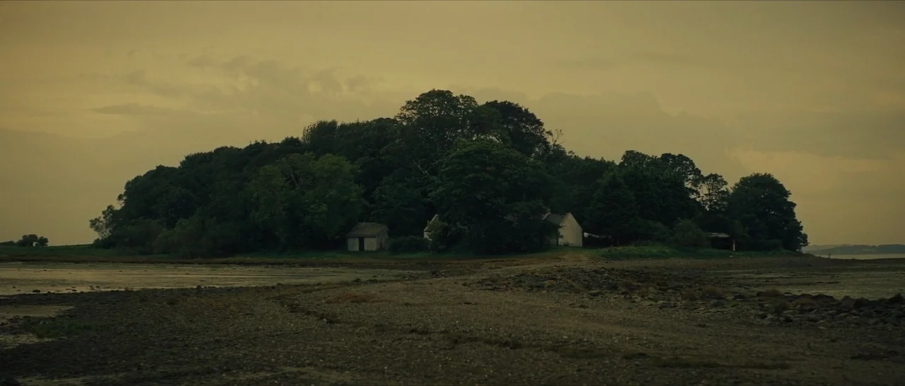 The Lost City of Z (2016) movie still: establishing — A low-lying island covered in dense trees sits in a tidal inlet at low tide. Small stone…