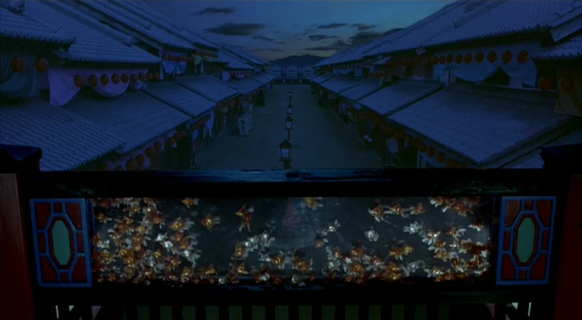 Sakuran (2006) movie still: establishing — A quiet Japanese plaza is flanked by traditional tiled-roof structures at twilight. A glass railing in…