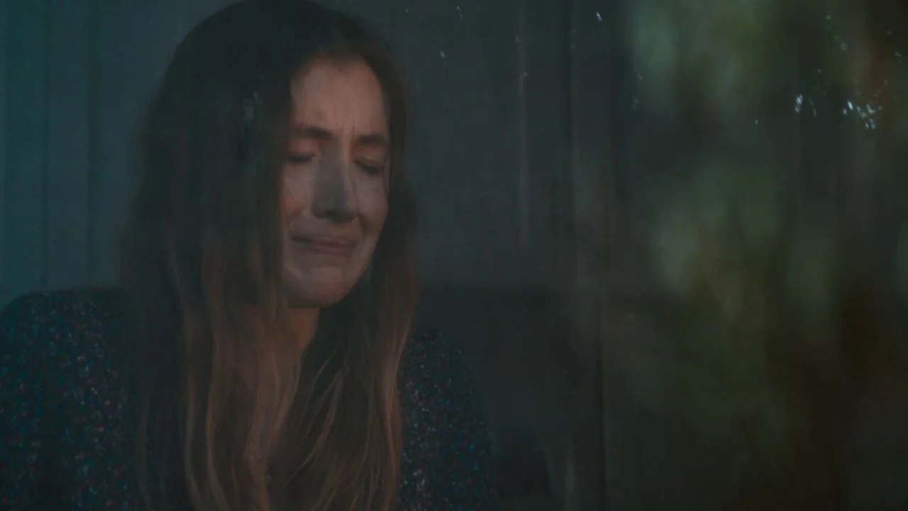 She Dies Tomorrow (2020) movie still: closeup — A woman stands in a dimly lit, dark space with obscured background details. The woman has her eyes…