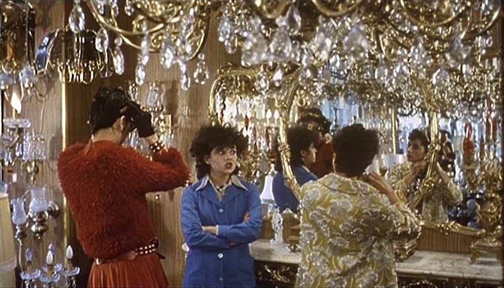 Labyrinth of Passion (1982) movie still: medium — A crowded showroom filled with numerous gold chandeliers and large mirrors covering the walls. Two…