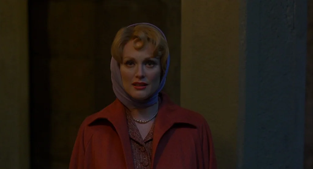 Far From Heaven (2002) movie still: closeup — A dark corridor features stone-like wall textures obscured by low ambient light levels. A woman stands…