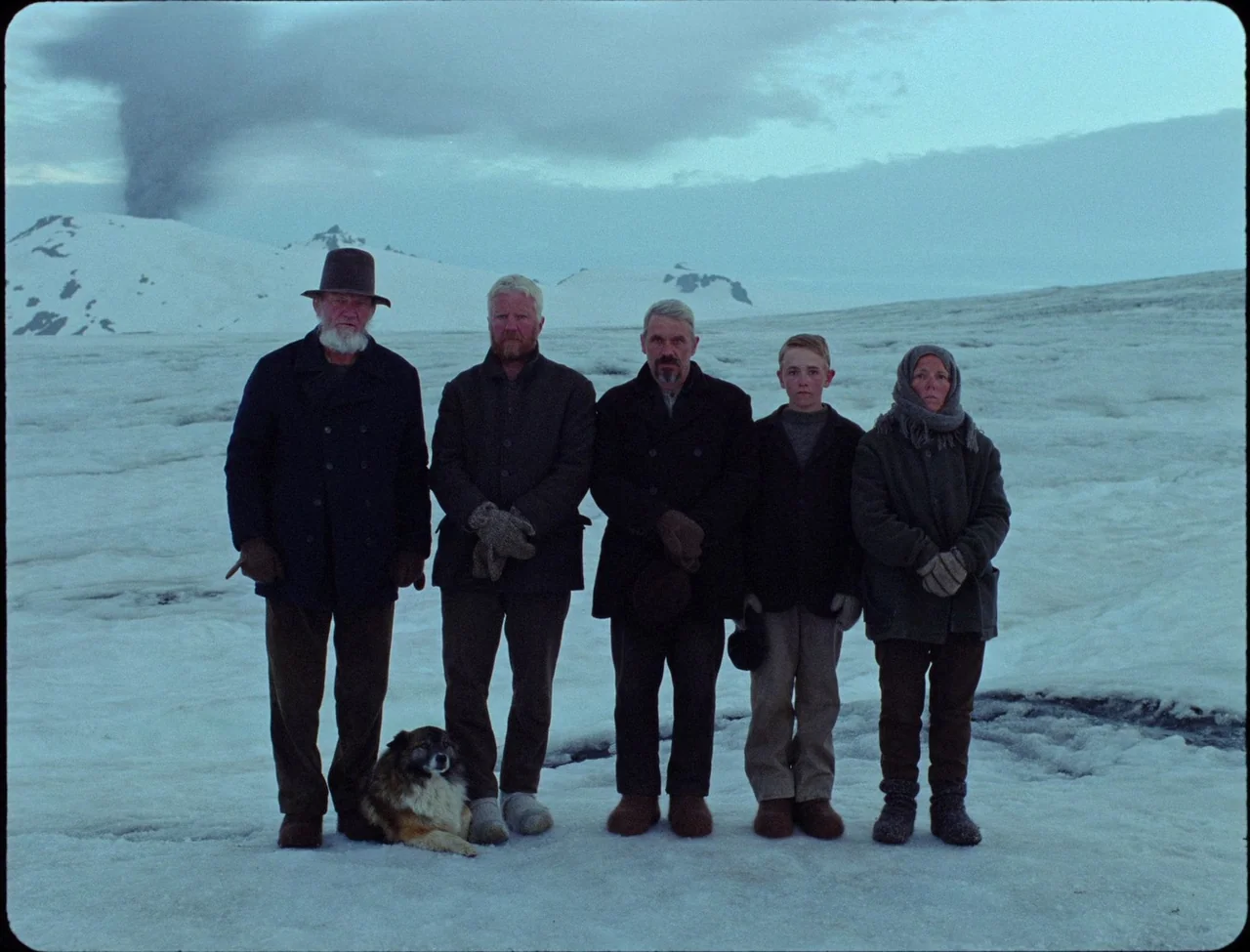 Godland (2022) movie still: fullbody — A group of five people and a small dog stand on an expansive icy glacier. Snowy mountains rise in the…