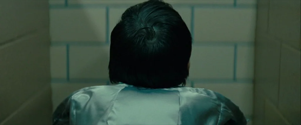 Let Me In (2010) movie still: closeup — A narrow space defined by light-colored, rectangular ceramic tiles with dark grout lines. A young person…