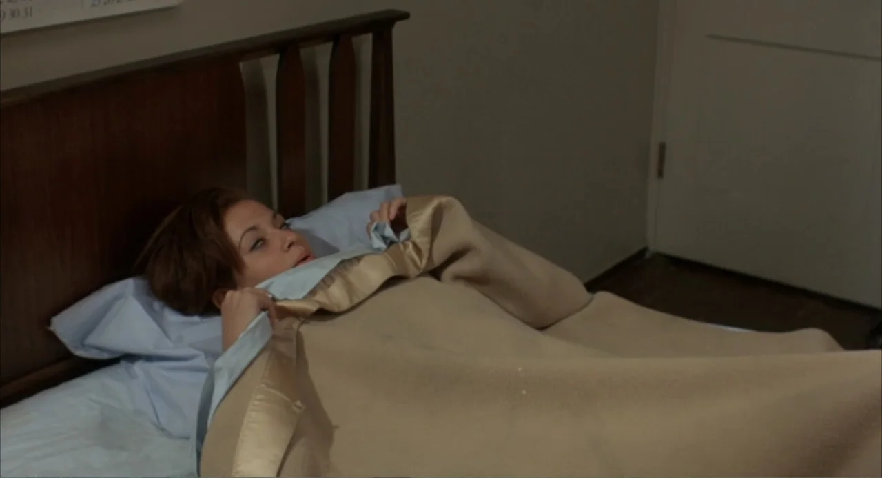Cooley High (1975) movie still: medium — A modest bedroom features a wooden headboard and light-colored wall. A young woman lies under a tan blanket…