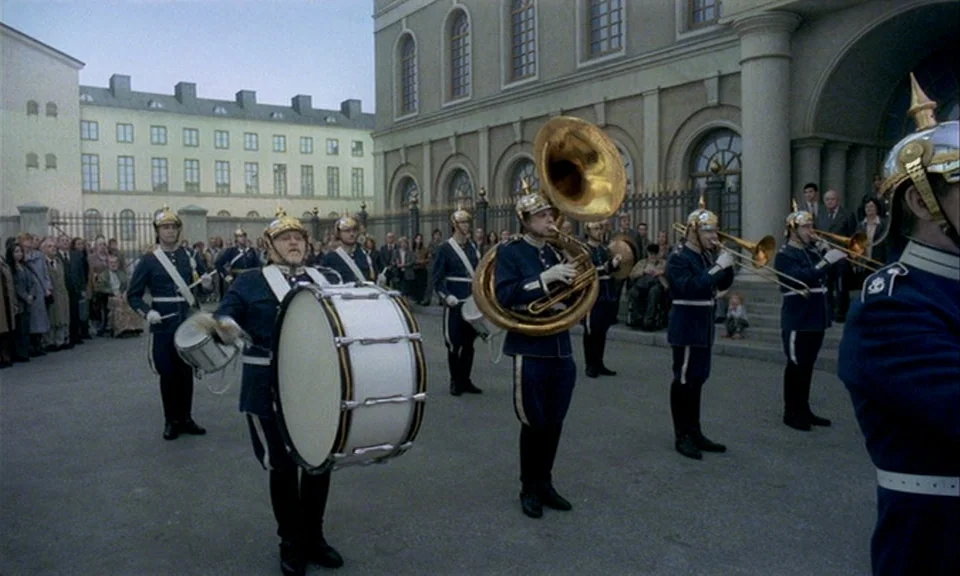 You, The Living (2007) movie still: wide — A group of musicians in vintage military uniforms plays instruments on a paved outdoor plaza. A large…