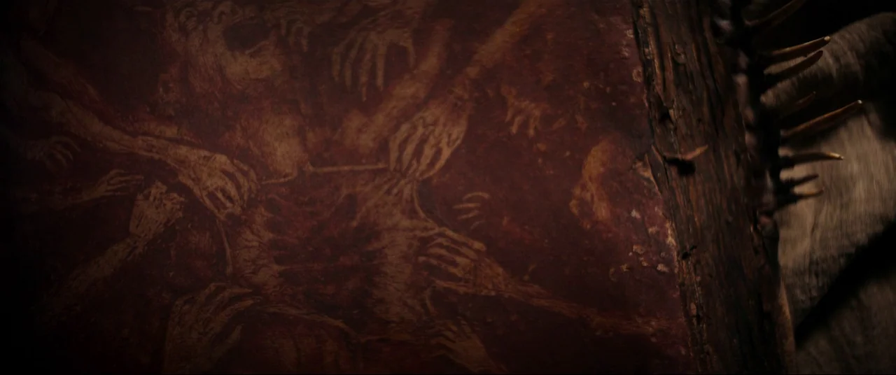 Evil Dead Rise (2023) movie still: closeup — A dark, worn leather book cover displays an etched illustration of many grasping hands. A spine with…