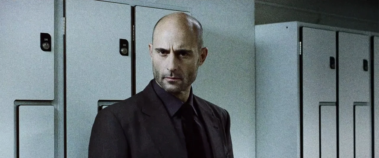 Anna (2013) movie still: medium — A locker room with rows of grey metal lockers containing numbered identification tags. A man stands in front of…