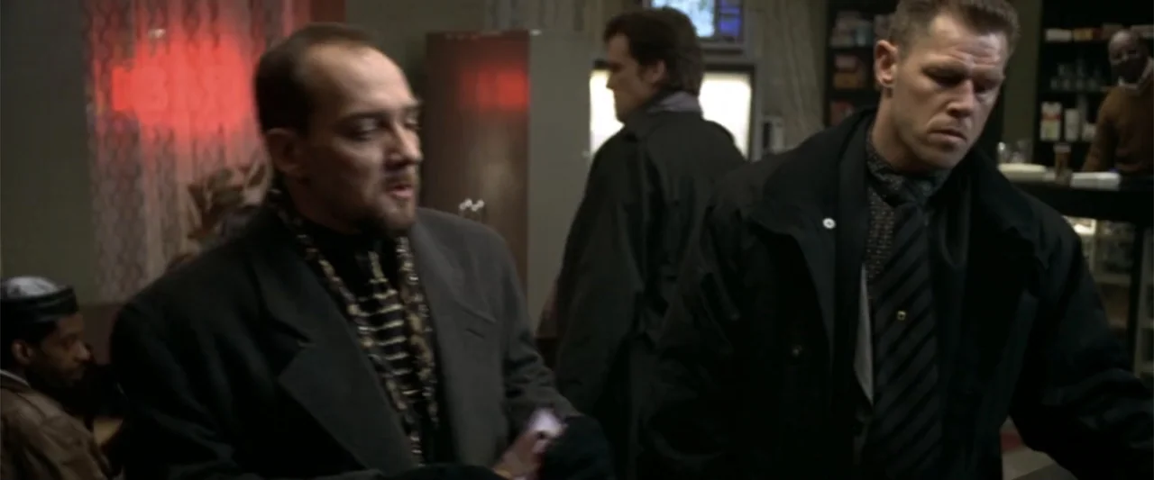 Maximum Risk (1996) movie still: medium — Two men talk inside a dimly lit 1990s-style diner with a red neon light. The men wear business attire…