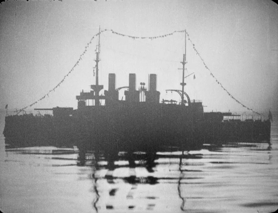 Battleship Potemkin (1925) movie still: wide — A battleship in silhouette floats on calm water against an overcast sky. Strings of signal flags hang…