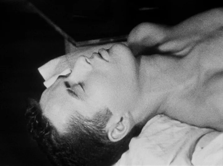 Fireworks (1947) movie still: closeup — A man lies on a flat surface in a medical examination room. The person remains motionless with eyes closed.