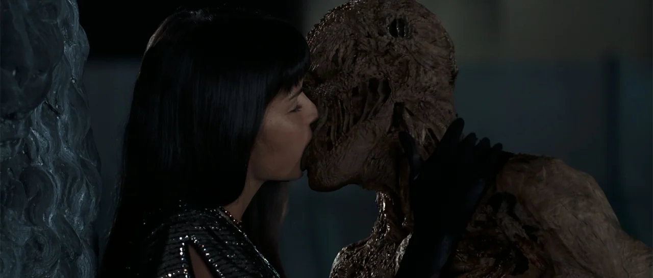 The Mummy Returns (2001) movie still: medium — A dark indoor space features a wall texture on the left side of frame. A woman with black hair kisses…