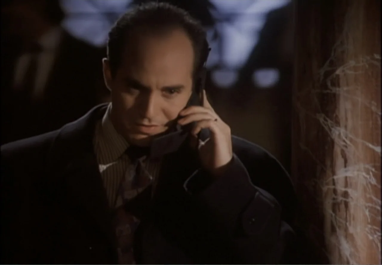 White Mile (1994) movie still: medium — A dimly lit room with a man standing beside a structural column. He holds a black mobile phone to his ear…