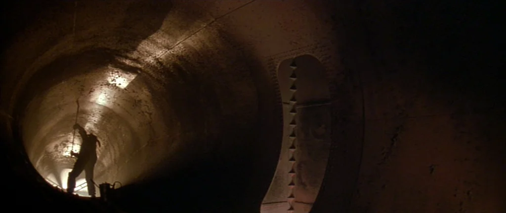 Alien 3 (1992) movie still: wide — A long cylindrical tunnel made of riveted metal sections curves into the darkness. A single figure stands against…