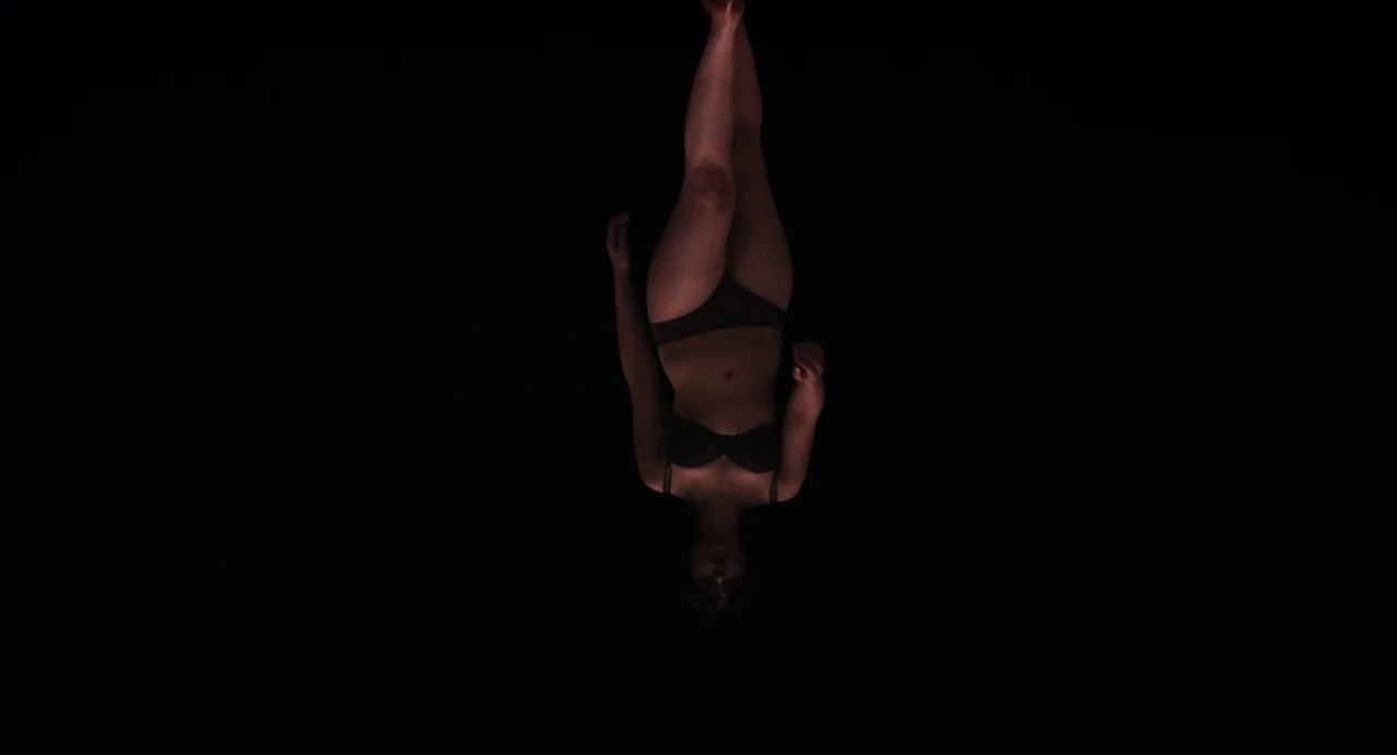 Under The Skin (2013) movie still: fullbody — A person floats in a completely black void with no visible floor or walls. The subject is oriented…