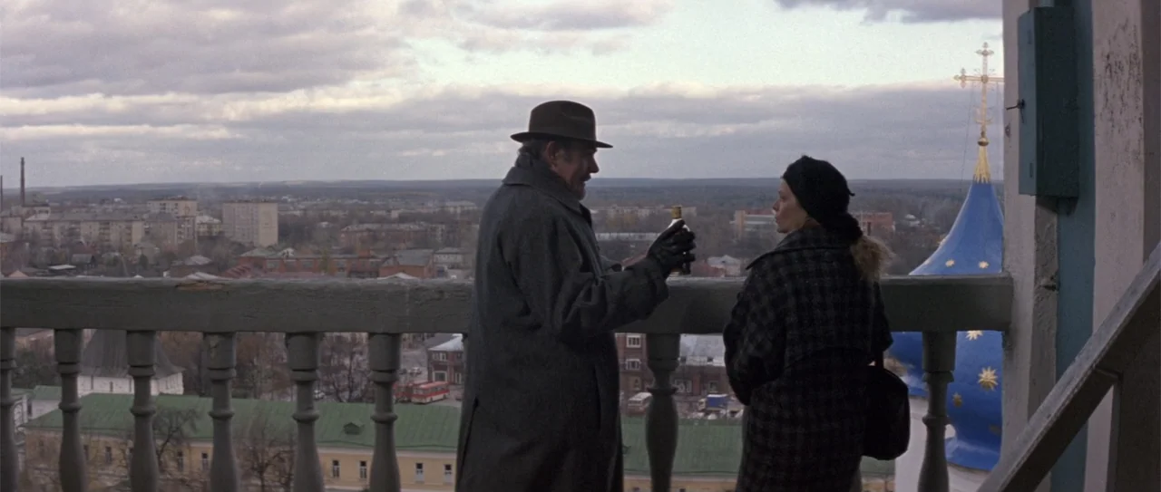 The Russia House (1990) movie still: fullbody — A stone balcony overlooks a distant cityscape with a blue onion-domed structure nearby. An older man…